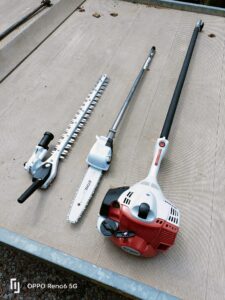 Trois accessoires STIHL pour débroussailleuse (taille-haie, élagueuse et tête à chaîne) posés sur une surface striée, avec signature "OPPO Reno6 5G".