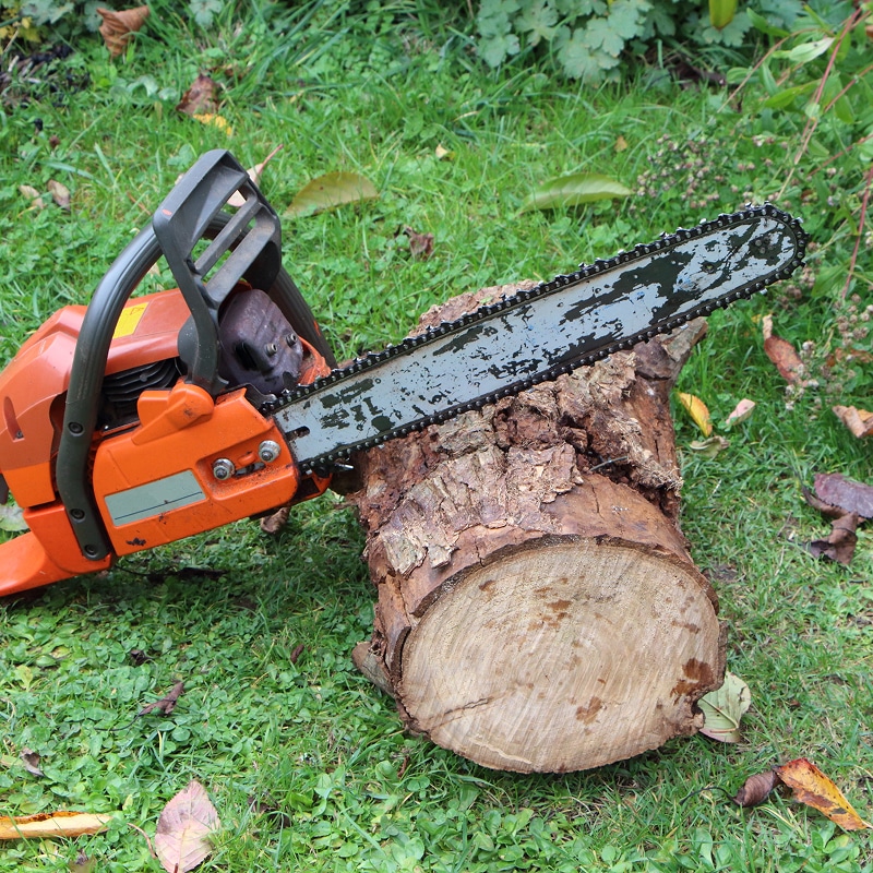 Tronçonneuse orange avec guide-chaîne usé positionné sur une bûche de bois coupée, posée sur une pelouse verte.